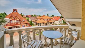A balcony with a table and chairs, overlooking a residential area with red-roofed houses.