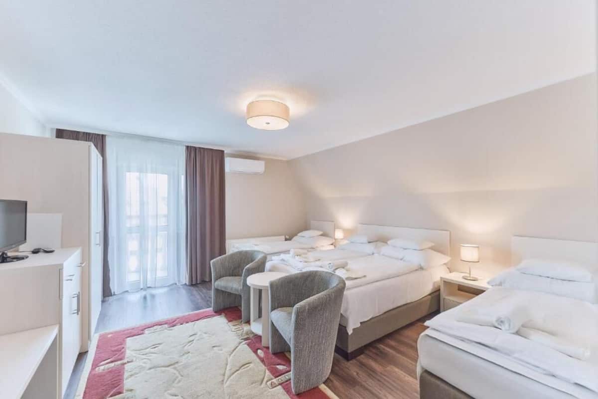 Une chambre d’hôtel comprenant un lit, deux fauteuils, un bureau, une télévision et une fenêtre avec des rideaux.