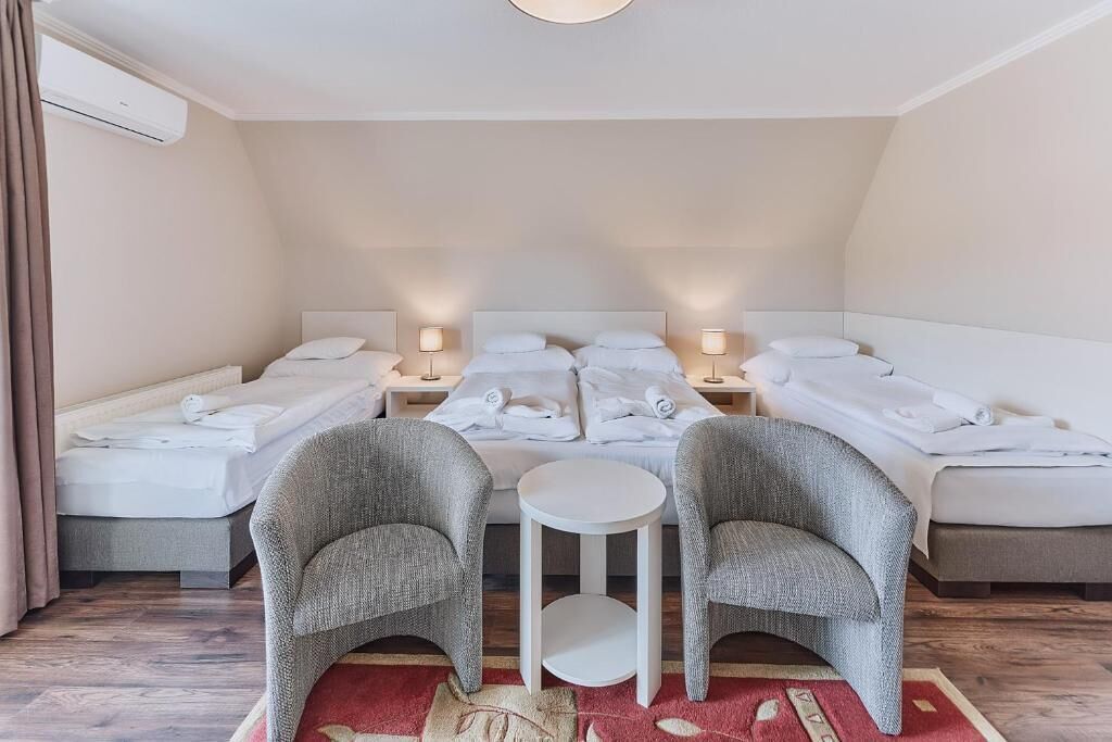 Une chambre d’hôtel avec deux lits, une petite table ronde, deux fauteuils et un tapis rouge.