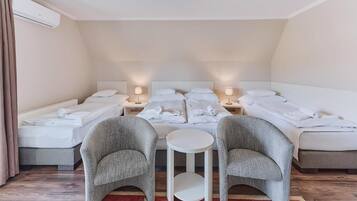 Une chambre d’hôtel avec deux lits, une petite table ronde, deux fauteuils et un tapis rouge.