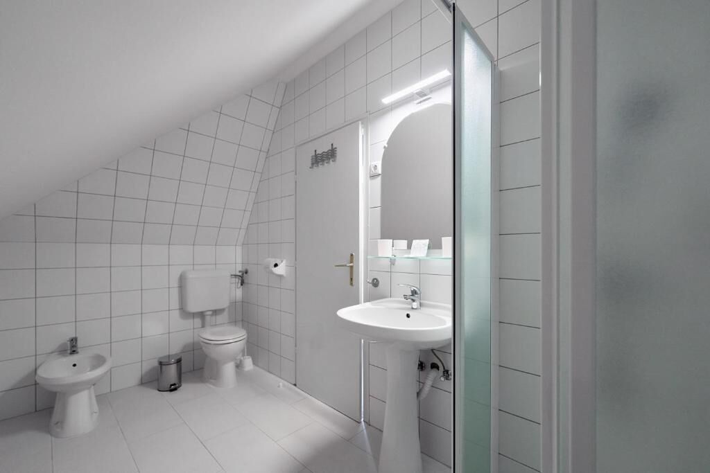 A modern bathroom with a toilet, bidet, sink, and a glass shower enclosure.