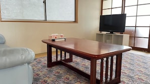 Une pièce avec une table en bois, un canapé, un téléviseur posé sur un meuble et un tapis à motifs.