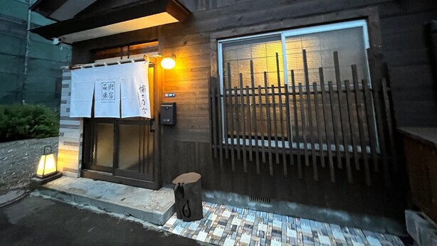 Un edificio de madera con un vestíbulo de baldosas, un farol y un letrero con caracteres japoneses.