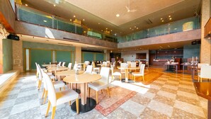 Amplio espacio interior con varias mesas y sillas de comedor, una zona de cocina y un nivel superior con barandillas de cristal.