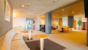 Un vestíbulo de hotel con un sofá curvo, una mesa redonda y una zona de comedor con sillas.
