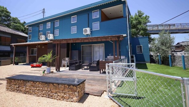 Una casa azul de dos pisos con un porche cubierto, mobiliario exterior y un patio cercado.