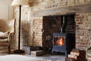 Une pièce rustique avec une cheminée en briques, un fauteuil en cuir, un lampadaire et un poêle à bois.