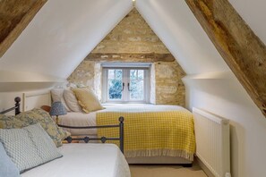 Een slaapkamer met een stenen muur, een raam, een bed met een geel geruit dekbed en een radiator.