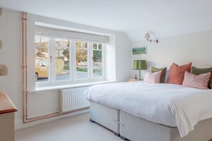 A bedroom with a large bed, a window with a view of a street, a radiator, and a bedside table with a lamp. - Luxury Family Period Home By The Cotswold Way (Leonard Stanley)