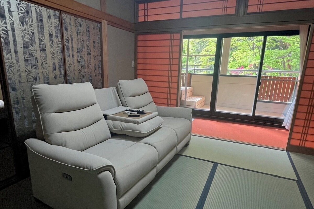 A room with a sofa, a sliding door, and a view of greenery outside.
