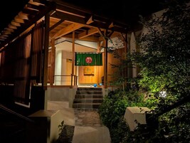 A traditional Japanese-style entrance with wooden beams, a stone staircase, and a green hanging sign.