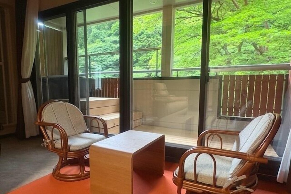 A room with two wicker chairs, a small wooden table, and a large window with a view of greenery.