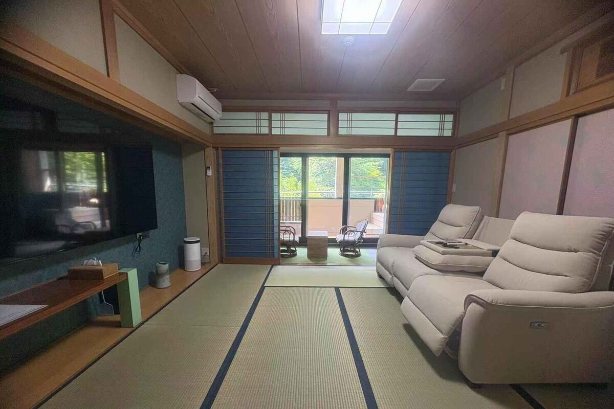 A living room with tatami flooring, a sofa, a television, and a sliding door leading to an outdoor area.