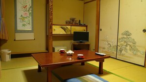 Una habitación japonesa tradicional con suelo de tatami, una mesa baja con juego de té, un televisor sobre un soporte y puertas correderas con una pintura floral.