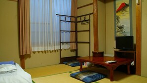 Una habitación japonesa tradicional con suelo de tatami, un futón, una mesa de madera baja, un televisor y un panel shoji.