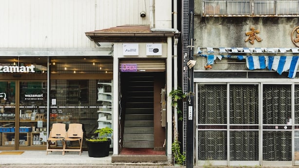 A storefront with a closed shutter, a neon 'OPEN' sign, and a blue and white striped awning. - Mitaya Micro Hotel (Suwa)