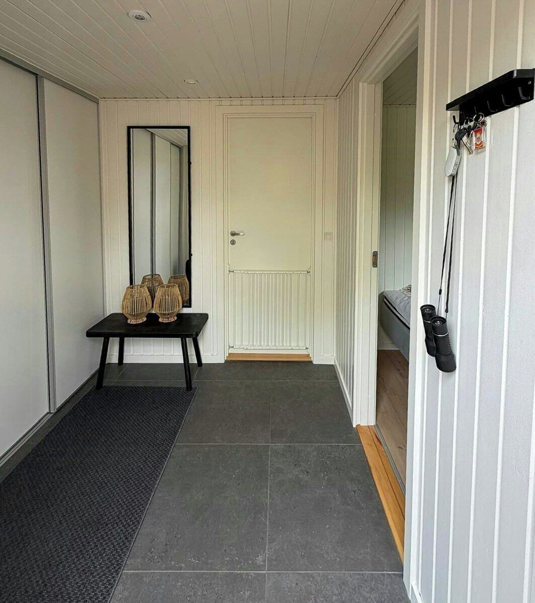 A hallway with a door, a mirror, a small table with decorative items, and a shoe rack.