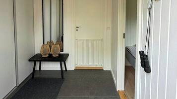 A hallway with a door, a mirror, a small table with decorative items, and a shoe rack.