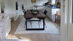 Uma sala de jantar com mesa e cadeiras de madeira, uma cozinha com armários brancos e teto branco.