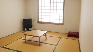 A room with tatami mat flooring, a wooden table, a television on a stand, and a window with a grid pattern. - Goemon Ryokan (Minamiuonuma)