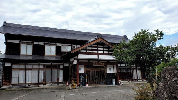 A traditional Japanese building with a wooden facade, large sliding doors, and a sign indicating a restaurant. - Goemon Ryokan (Minamiuonuma)