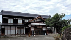 A traditional Japanese building with a tiled roof, wooden beams, and a signboard. - Goemon Ryokan (Minamiuonuma)