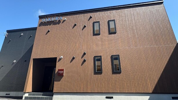 A building with a wooden facade, a sign reading 'SAKURA,' and a door. - Sakura Shinkawa (Sapporo)