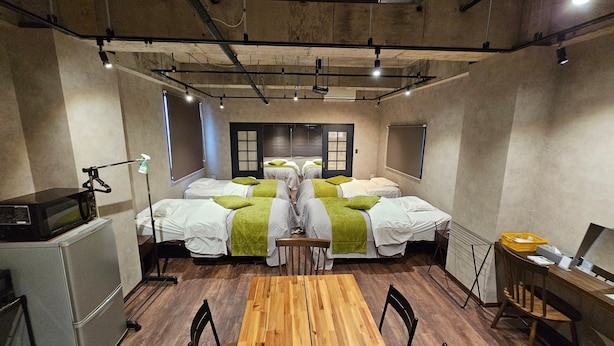 A room with four beds, a desk, a chair, a microwave, and a small table with a basket.