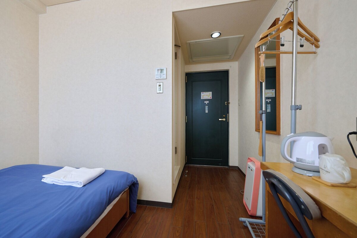 Habitación de hotel con cama, escritorio con tetera, espejo y puerta que da a otra habitación.