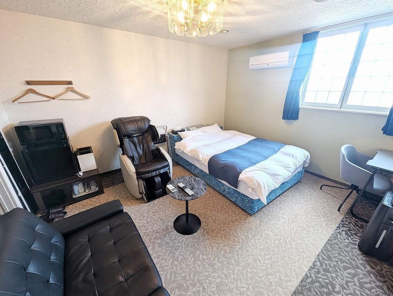 A hotel room with a bed, a massage chair, a small table, a desk, and a TV.