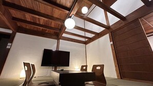 Una habitación con techo de madera, televisor de pantalla plana, una mesa y cuatro sillas.