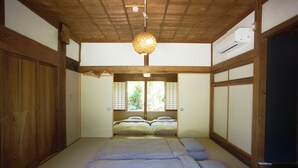 Una habitación japonesa tradicional con suelo de tatami, futón, puertas correderas y una lámpara colgante.
