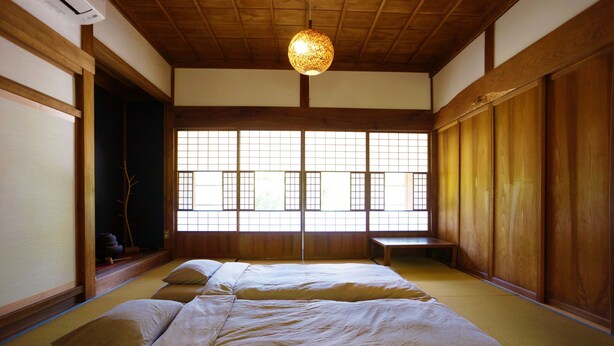 Una habitación japonesa tradicional con suelo de tatami, una cama de madera baja y un amplio ventanal con vistas a la vegetación.