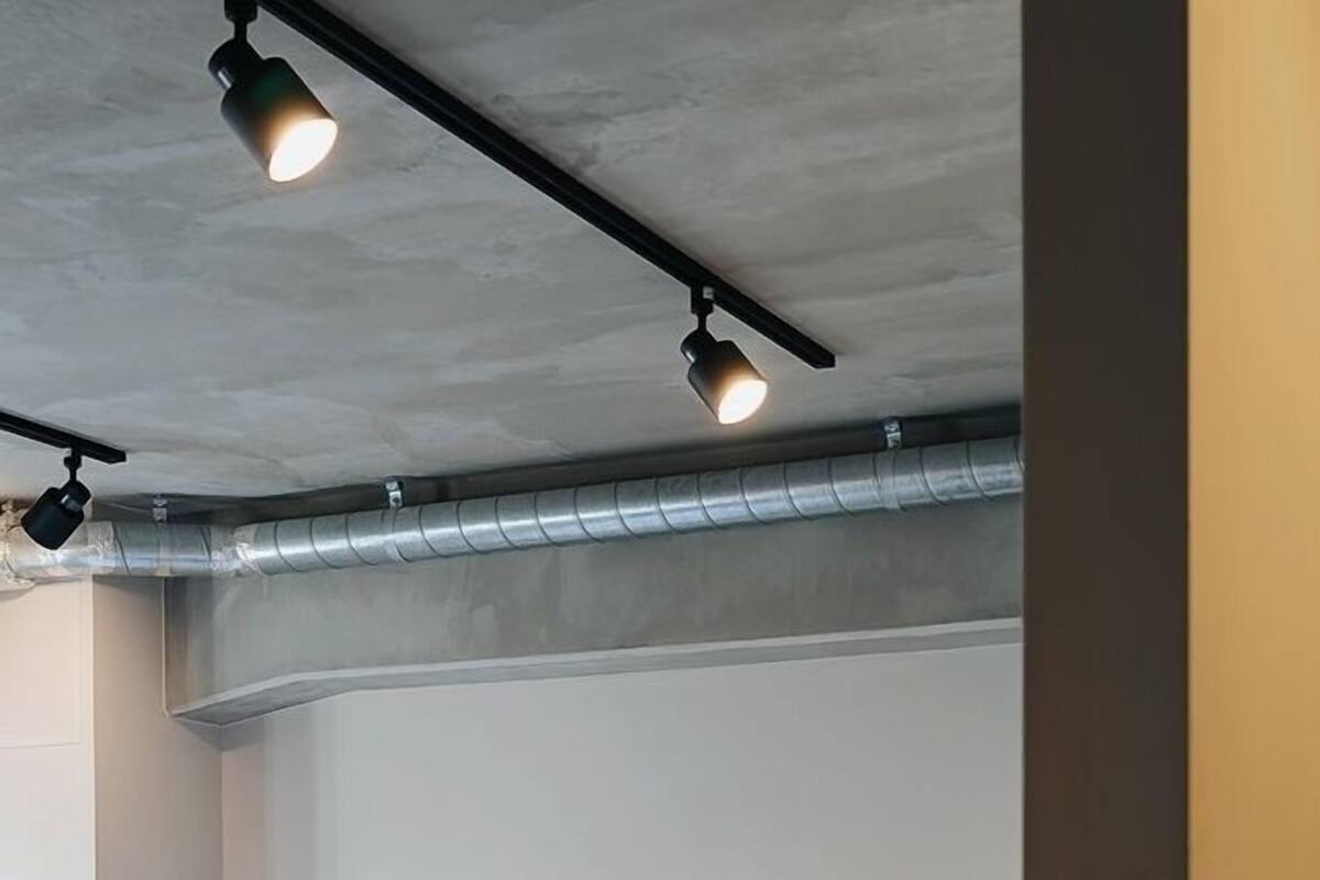 Une chambre avec deux lits simples, un plafond en béton et des conduits apparents.