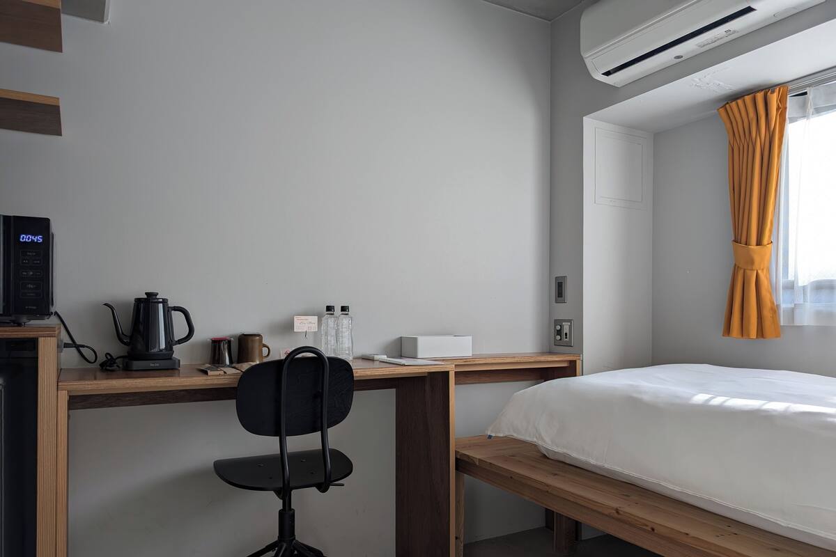 Une chambre avec un lit, un bureau et une chaise, une machine à café et une bouilloire.