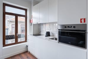Eine moderne Küche mit weißen Schränken, einem schwarzen Backofen und einem Fenster mit Blick auf Gebäude.