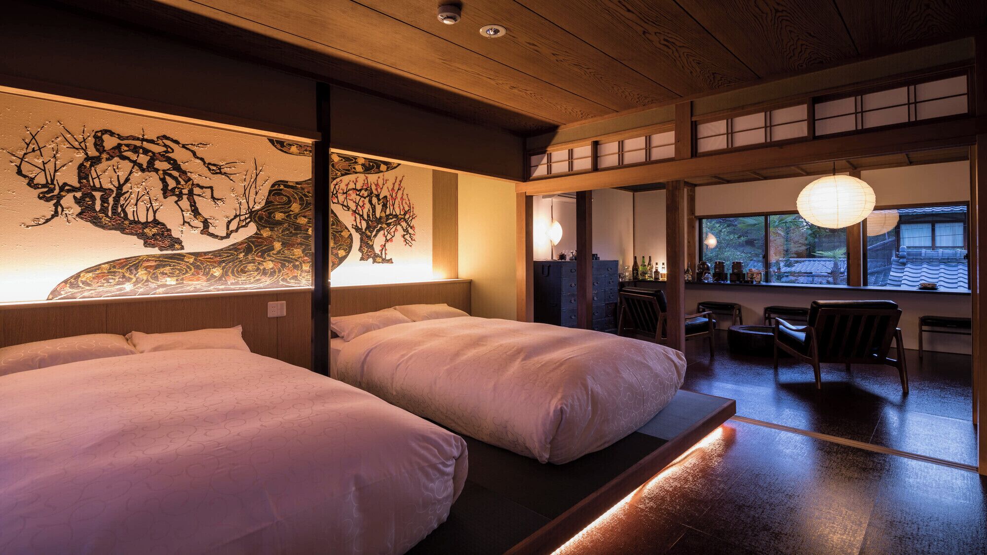 Ein traditioneller japanischer Raum mit zwei Betten, einer Holzbalkendecke und Blick ins Freie durch ein Fenster.