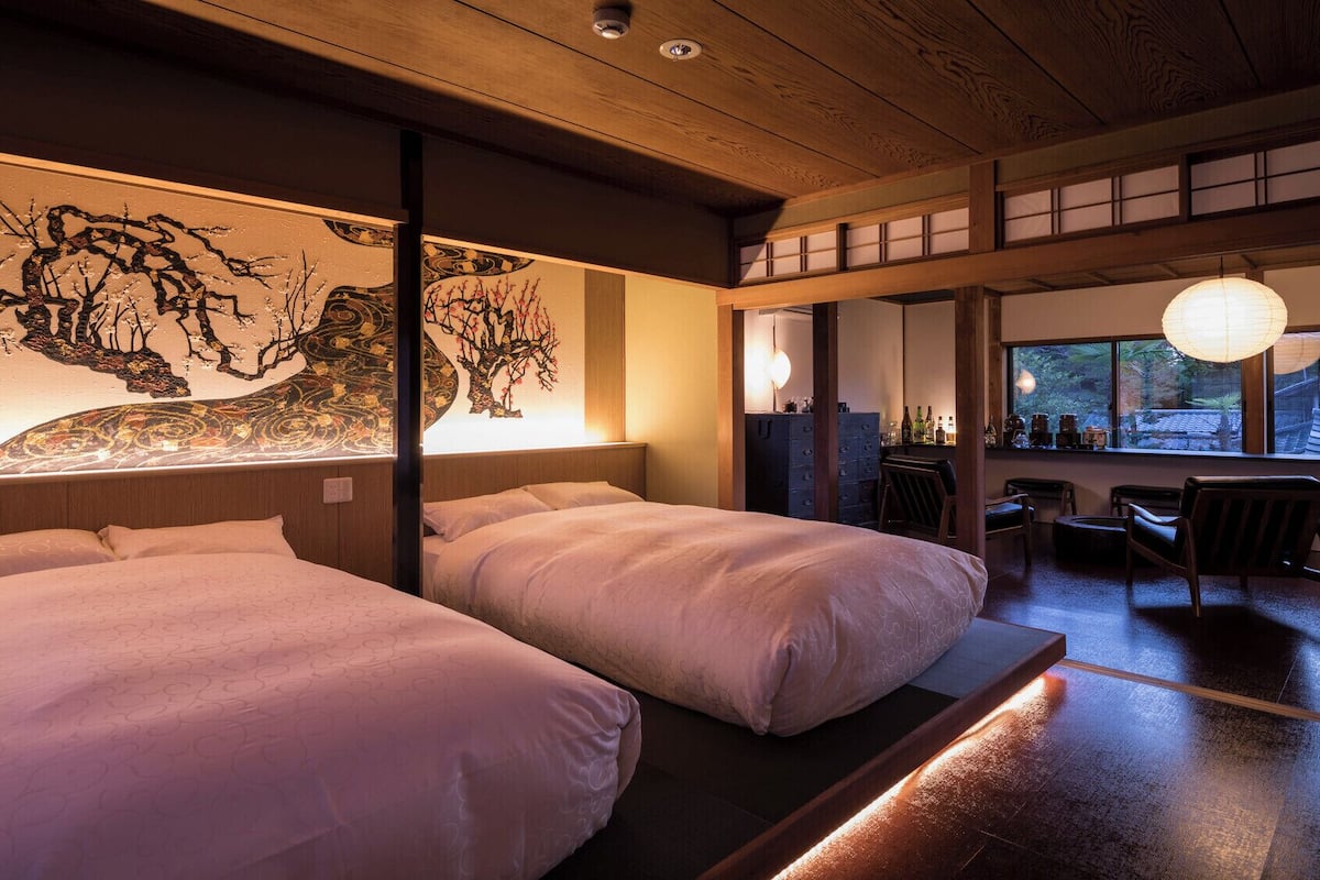 Ein traditioneller japanischer Raum mit zwei Betten, einer Holzbalkendecke und Blick ins Freie durch ein Fenster.