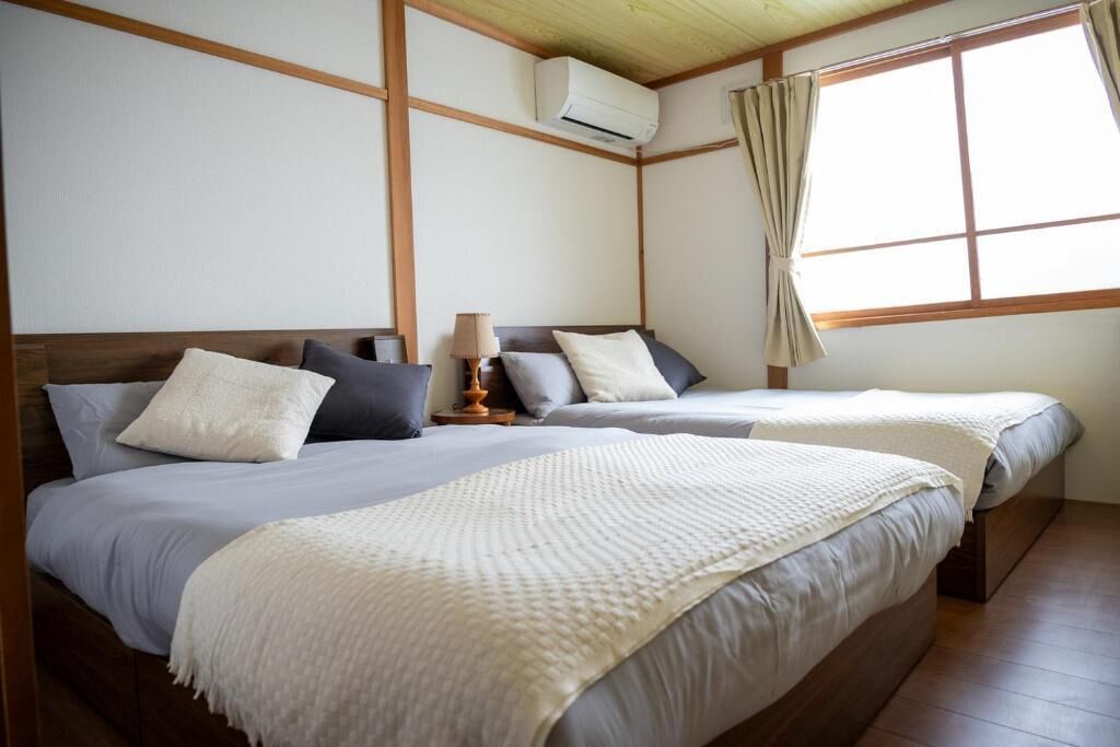 Ein Hotelzimmer mit zwei Betten, einem Fenster mit Vorhängen, einer Klimaanlage und einer Holzbalkendecke.