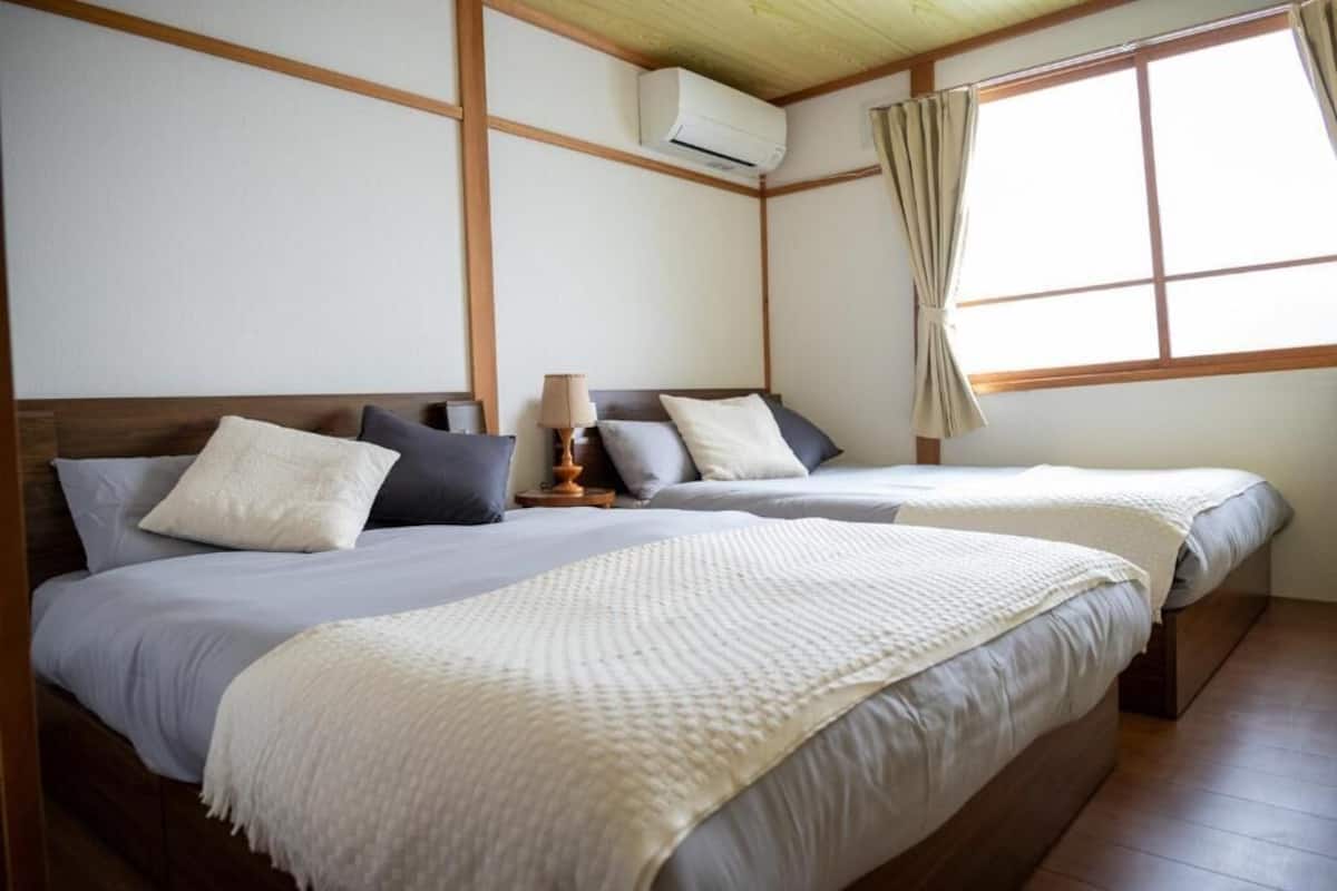 A hotel room with two beds, a wooden ceiling, an air conditioning unit, and a window with curtains.
