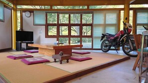 Una habitación con tatami, mesa de madera, cojines, televisor y una motocicleta.