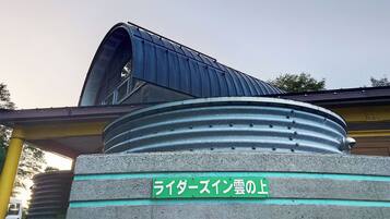 A building with a curved metal structure, a green sign with Japanese characters, and a concrete base.