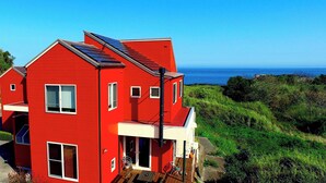 A red two-story house with solar panels, a balcony, and a view of the ocean. - Pension C-cabin (Minamiboso)