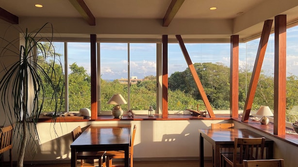 A spacious room with large windows, wooden beams, and a dining table with chairs. - Pension C-cabin (Minamiboso)
