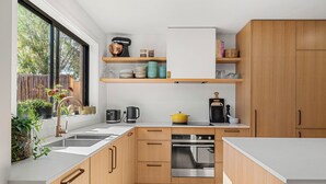 A modern kitchen with wooden cabinets, a stainless steel oven, and a window with plants. - Central and very close to retail hub, restaurants, cafes, Coles, Woolworths (Cowes)
