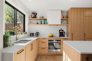 A modern kitchen with wooden cabinets, a stainless steel oven, and a window with plants. - Central and very close to retail hub, restaurants, cafes, Coles, Woolworths (Cowes)