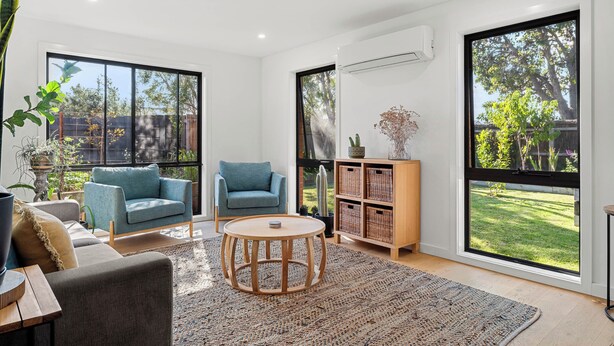 A modern living room with a sofa, armchair, round coffee table, and a large window with a view of a garden. - Central and very close to retail hub, restaurants, cafes, Coles, Woolworths (Cowes)
