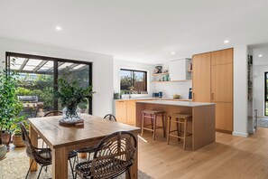 A modern kitchen with wooden cabinets, a central island, and a dining area with a wooden table and chairs. - Central and very close to retail hub, restaurants, cafes, Coles, Woolworths (Cowes)