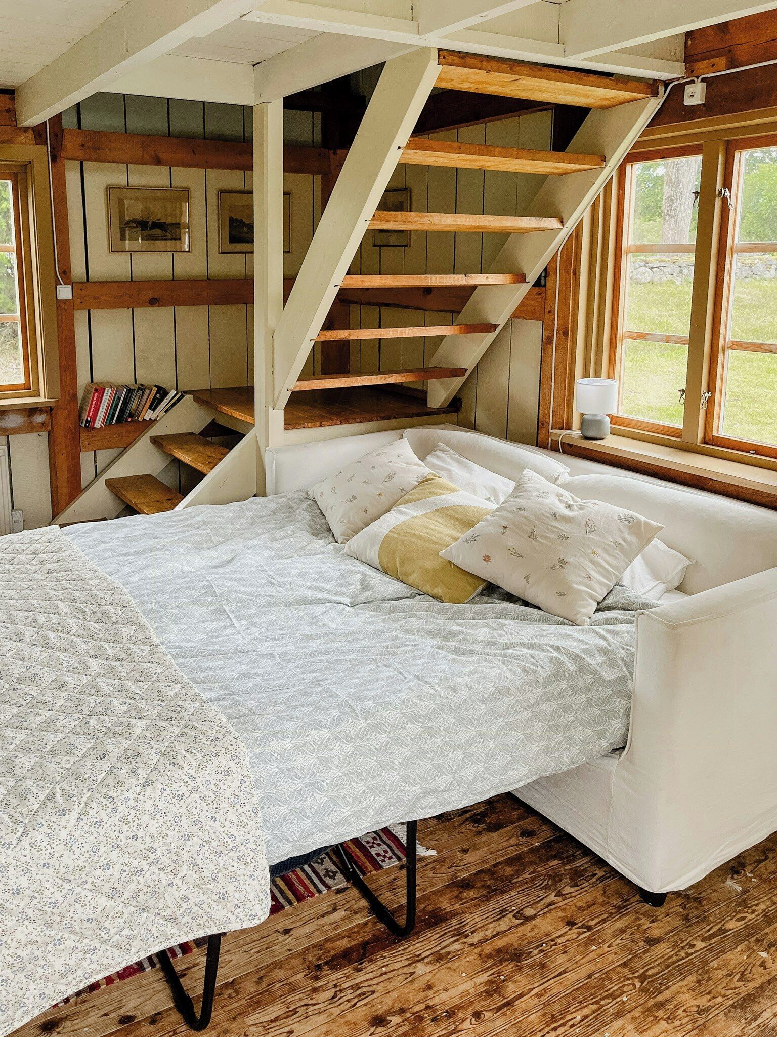 A bedroom with a bed, a window, a staircase, and wooden beams.