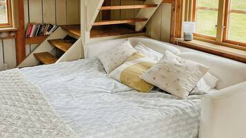 A bedroom with a bed, a window, a staircase, and wooden beams.